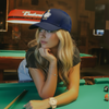 "Gorra azul DUCK U estilo streetwear modelada por mujer en mesa de billar"